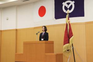 辞令交付式であいさつを行う市長の写真です。写真中央の壇上でマイクに向かってしゃべっています。