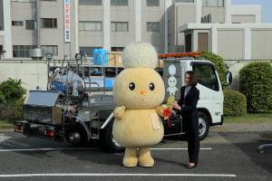 お披露目式の写真です。新しく配備された給水車の前で、市キャラクターぽぽたんから、車のキーのレプリカを市長が受け取っています。