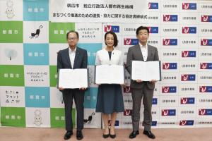 協定書締結式の記念写真です。URの担当者と松下市長が、協定書を手にバックパネルの前に立っています。
