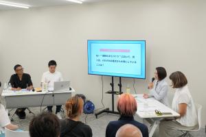 トークセッションの様子です。テーマが映し出されたモニターを中心に、参加者がマイクを手に意見を述べています。