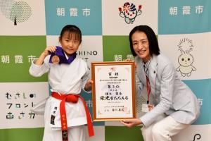 表敬訪問の記念写真です。市のバックパネルの前で、榎本選手と松下市長がメダル・賞状を手にして、にこやかに写っています。
