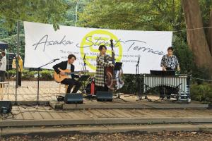 ストリートテラスの様子です。市役所近くの芝生広場に設けられたウッドデッキで、アコースティックギター、チェロ、ビブラフォンのアンサンブルが行われています。