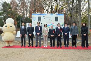 落成式の記念写真です。設置されたトイレトレーラーの前で、市長をはじめ、トイレトレーラーの所有者などの来賓が立っています。