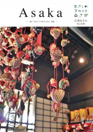 広報あさか令和8年3月号の表紙画像です。表紙は根岸台にある国指定重要文化財、旧高橋家住宅で毎年実施している、ひなかざりやつるしびなの様子です。背景に七段かざりのひなかざりがあり、手前に大きくつるしびなが写っています。