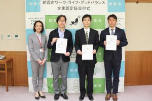 認定証交付式の記念写真です。朝霞市のバックパネルの前に市長と認定を受けた各企業の代表者が認定証を手にして写っています。