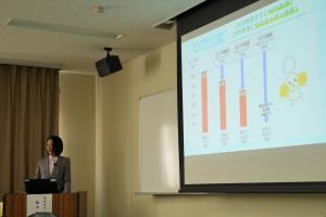 キックオフイベントで温室効果ガス等について説明をする市長の写真です。スライドを画面に投影し説明を行っています。