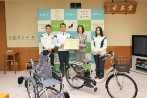 感謝状贈呈式の記念写真です。寄贈された電動自転車と車いすを前に並べ、テイエステックの社長・社員が松下市長と感謝状を手に写っています。
