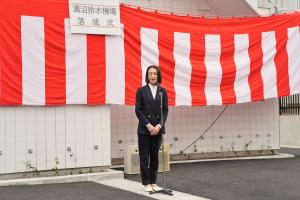 落成式の様子の写真です。紅白幕の前で、松下市長が参加者に向けてあいさつを行っています。