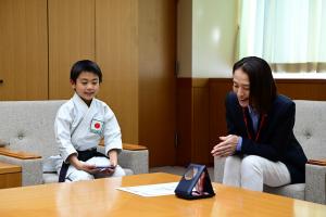 表敬訪問の様子の写真です。松下市長と三村選手が表彰メダルを見ながら、大会の思い出を話しています。
