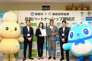 パートナーシップ締結式の記念写真です。飯能信用金庫の役員の方と市長が締結書を手に写っています。市キャラクター・飯能信用金庫キャラクターも一緒です。