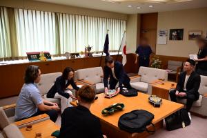 表敬訪問の様子の写真です。テーブルの上に並べられたチャンピオンベルトを手にして、市長がボクシングジムの関係者から説明を受けています。