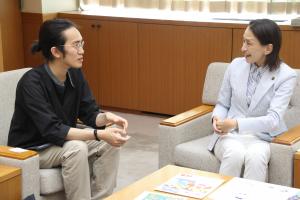表敬訪問の様子の写真です。じゅうきゅうさいさんと松下市長がテーブルに並べられた原画等を手に笑顔で談笑しています。