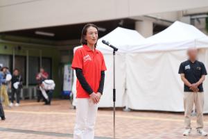 開会式でのあいさつの写真です。総合体育館前の特設ブースで市長がマイクの前に立ち、あいさつを行っています。